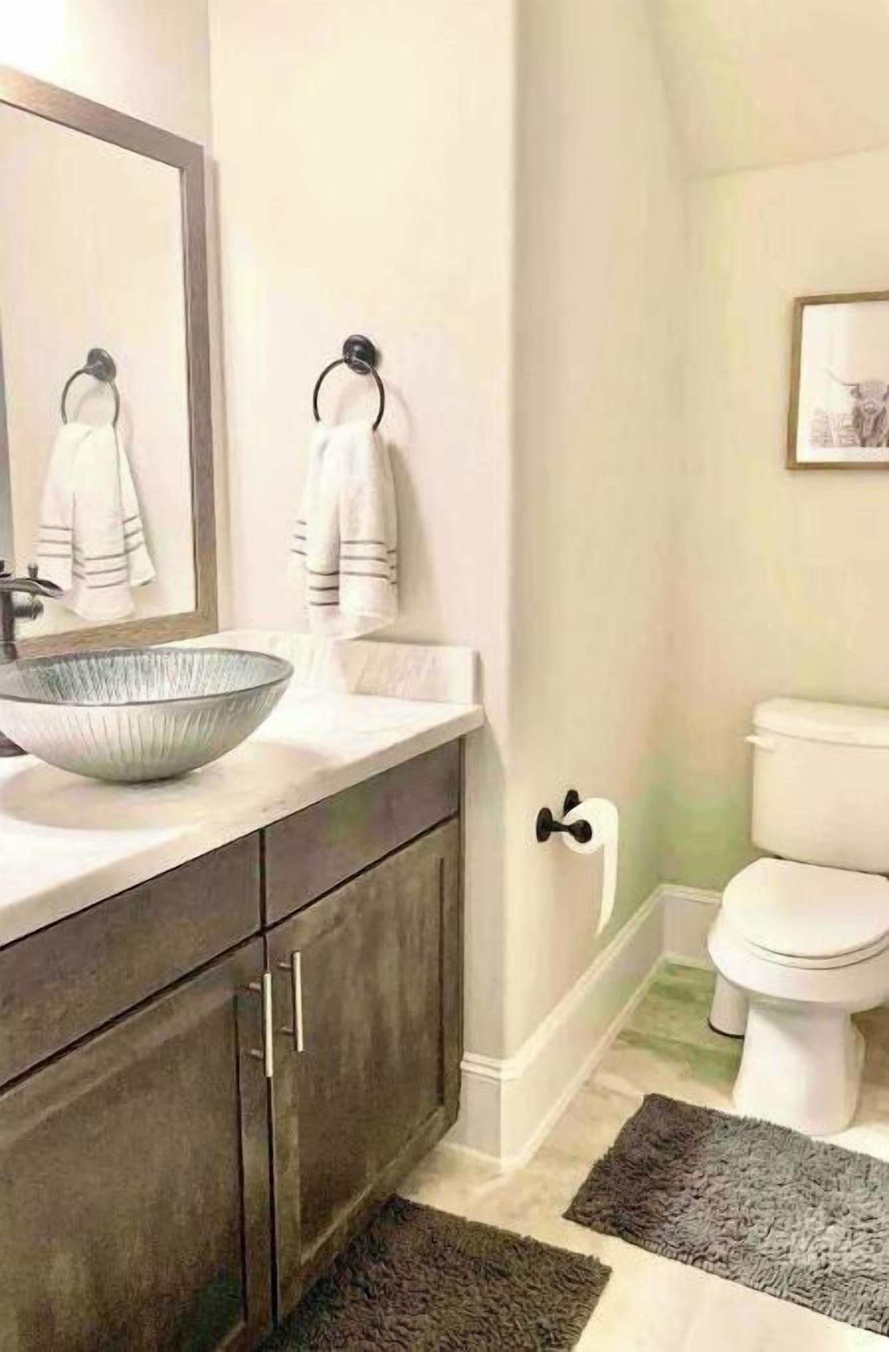 Ein Badezimmer mit einem großzügigen Vessel-Waschbecken, dunklen Holzschränken, einer weißen Toilette und einem gerahmten Bild an der Wand.