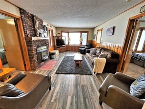 A cozy living room with a fireplace, leather sofas, a TV, and a dining area. - Butternut Lake Front Home, sleeps 6 (Butternut)