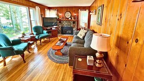 Ein gemütliches Wohnzimmer mit Holzwänden, einem Steinkamin, einem Fernseher und bequemen Sitzmöglichkeiten.