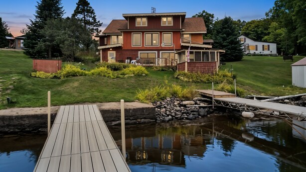 A two-story house with a dock extending into a pond, surrounded by greenery and trees. - Lakeview Retreat, Lakeside on the Flowage (Butternut)