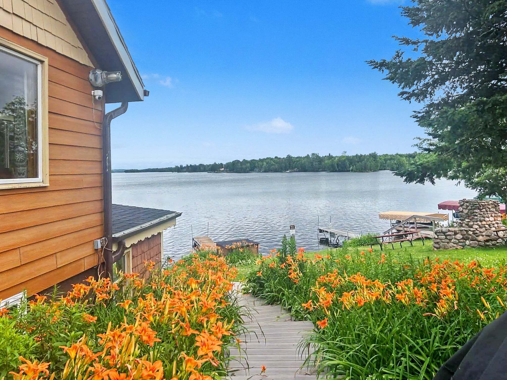 Una casa di legno con un molo che si estende su un lago tranquillo, circondata da fiori arancioni vivaci e una struttura in pietra.