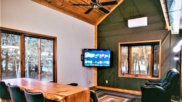 Una habitación acogedora con una mesa de comedor de madera, sillas negras, un sofá y un televisor montado en la pared.