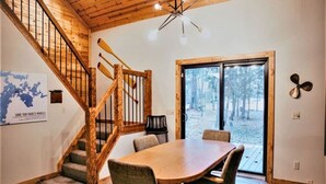 Una escalera de madera con vistas al exterior, un comedor con mesa y sillas, y un gran ventanal.