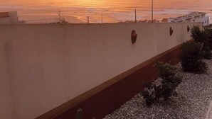 A sunset view from a balcony overlooking a beach with a low wall and street lamps. - Mom Home-007 (caldas da Rainha)