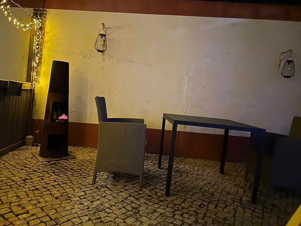 Een gezellig buitenzitgedeelte met een rieten stoel en een tafel, een kleine heater en lichtslingers aan de muur.