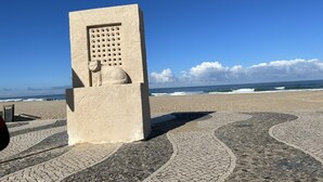 A stone structure with a carved cat and a grid pattern, located on a cobblestone path by the beach. - Mom Home-007 (caldas da Rainha)