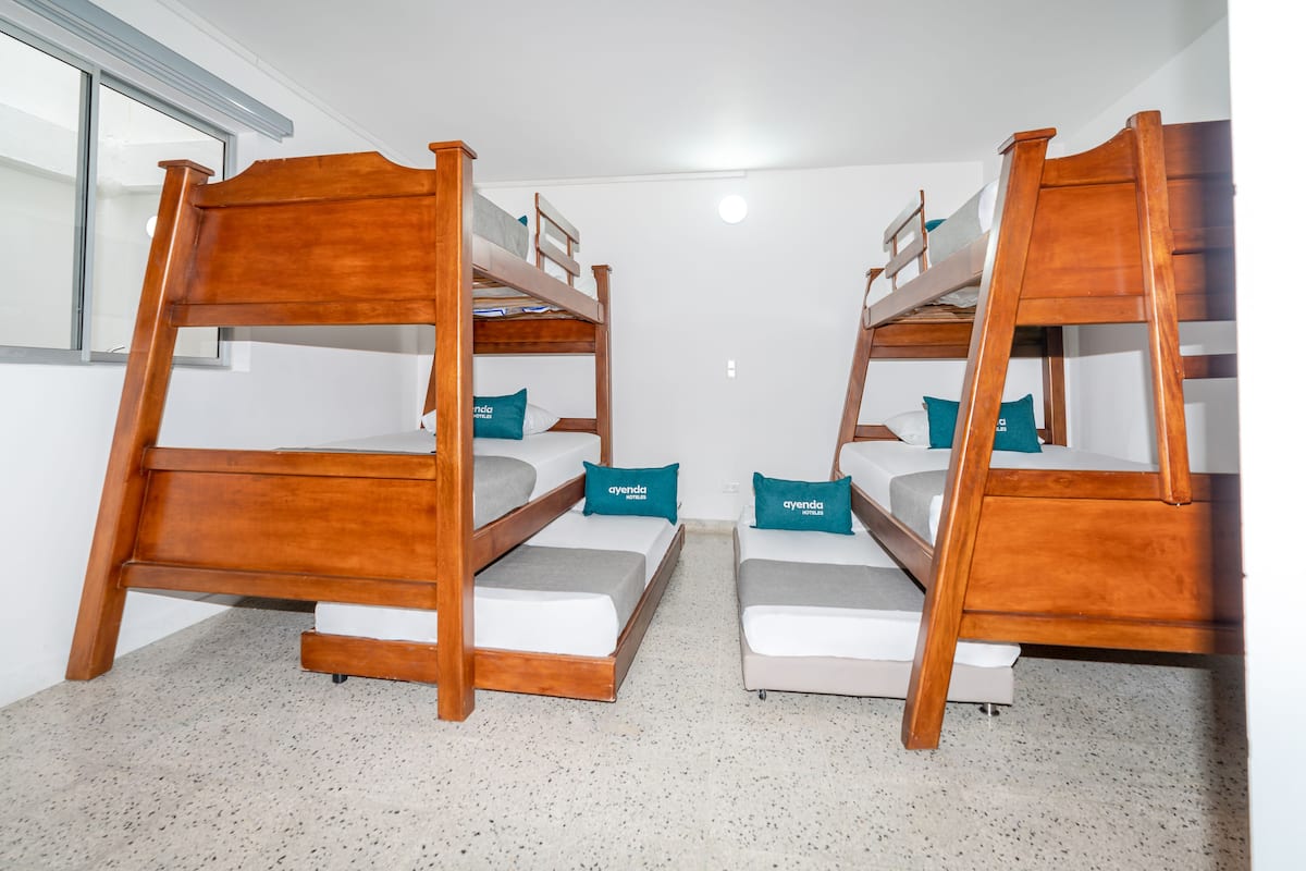 Una habitación con dos literas de madera, cada una con colchón y almohadas, y un ventanal pequeño.