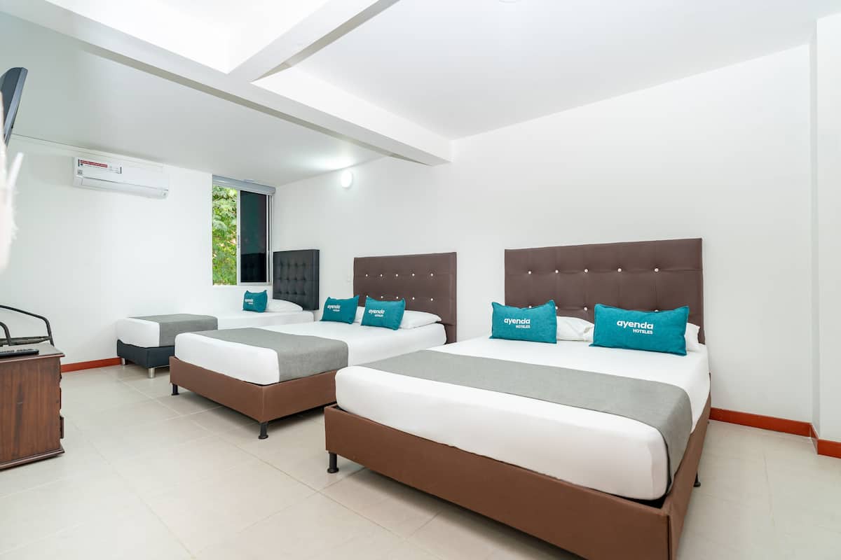Habitación de hotel con tres camas, un escritorio y una ventana con vista a zonas verdes.