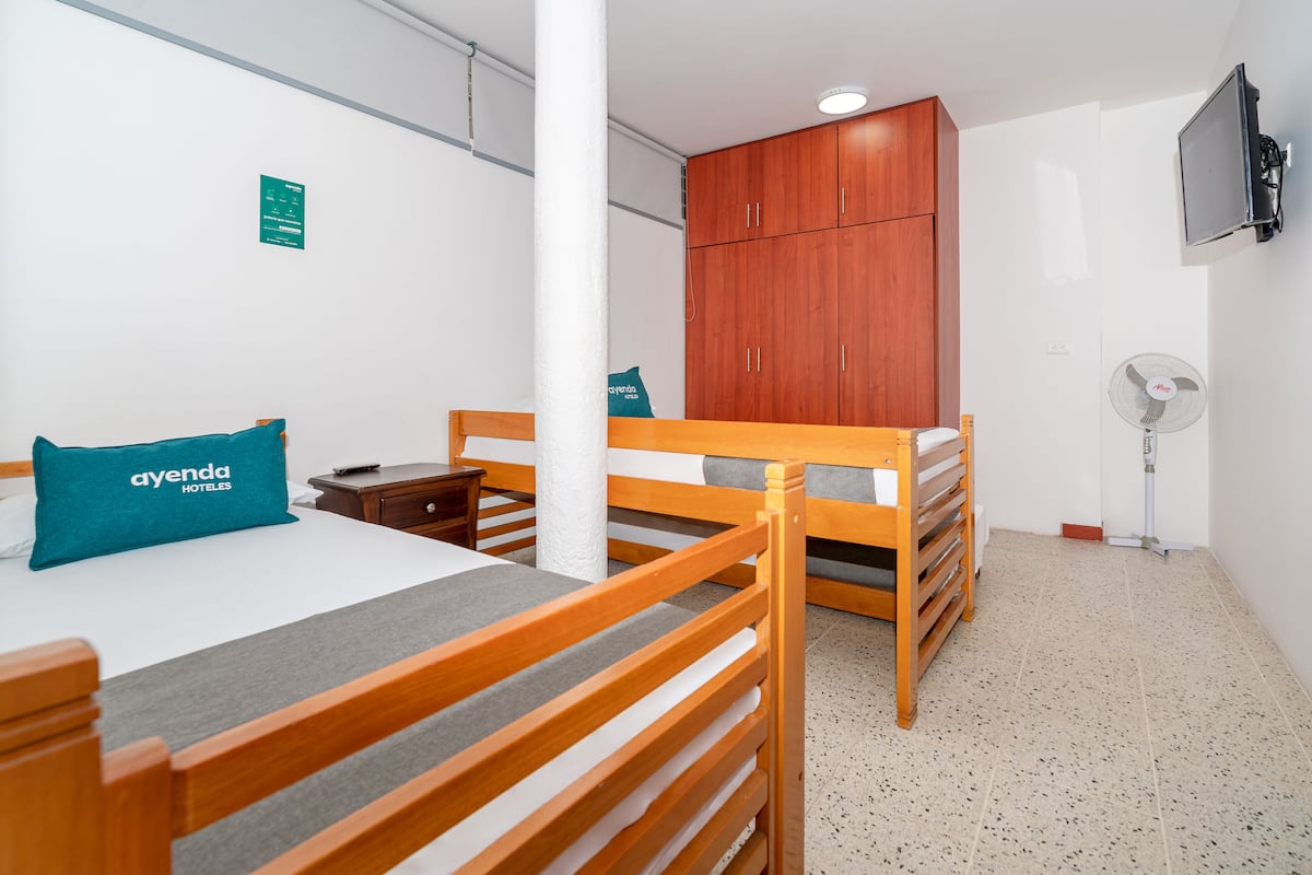 Habitación de hotel con cama, armario de madera, escritorio, silla, almohada, ventilador y televisor.
