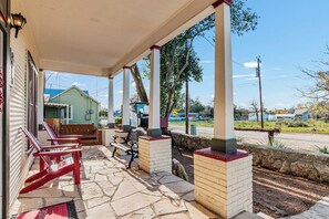 Un porche cubierto con suelo de piedra, muebles de exterior rojo y negro, y vista a una zona residencial con casas y una calle.