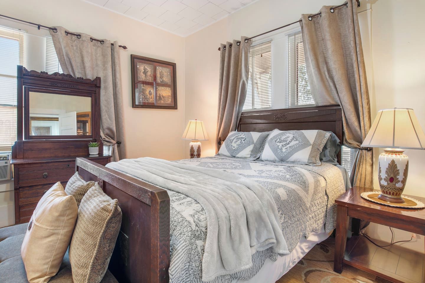 A bedroom with a wooden bed, a dresser, a mirror, a bedside table with a lamp, and a window with curtains.
