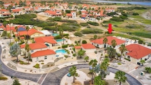 Zona residencial costera con casas de techos rojos, rodeada de vegetación y una playa.