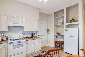 A kitchen with white cabinetry, a stove, a coffee maker, and a refrigerator.