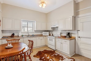 A kitchen with white cabinetry, a dining table with chairs, a cowhide rug, and a ceiling fan. - Carriage Inn - Bandera Suite 2 (Bandera)