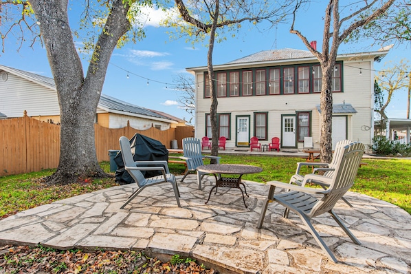 A backyard patio with stone flooring, outdoor furniture, and a house in the background. - Carriage Inn - Bandera Suite 2 (Bandera)