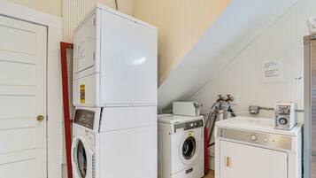 A laundry room with a front-loading washer, a stacked dryer, and a coin-operated washing machine.
