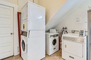 A laundry room with a front-loading washer, a stacked dryer, and a coin-operated washing machine.