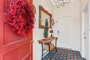 A hallway with a red door, a mirror, a small Christmas tree, and a patterned rug.