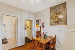A dining area with a wooden table and chairs, a vase with flowers, a painting on the wall, and a staircase leading to another room.