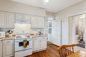 A kitchen with white cabinetry, a stove, a microwave, and a coffee maker.