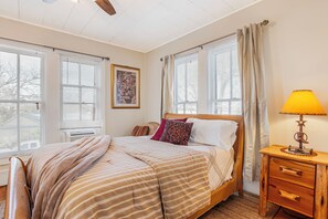 A bedroom with a bed, bedside table, lamp, and windows with blinds.