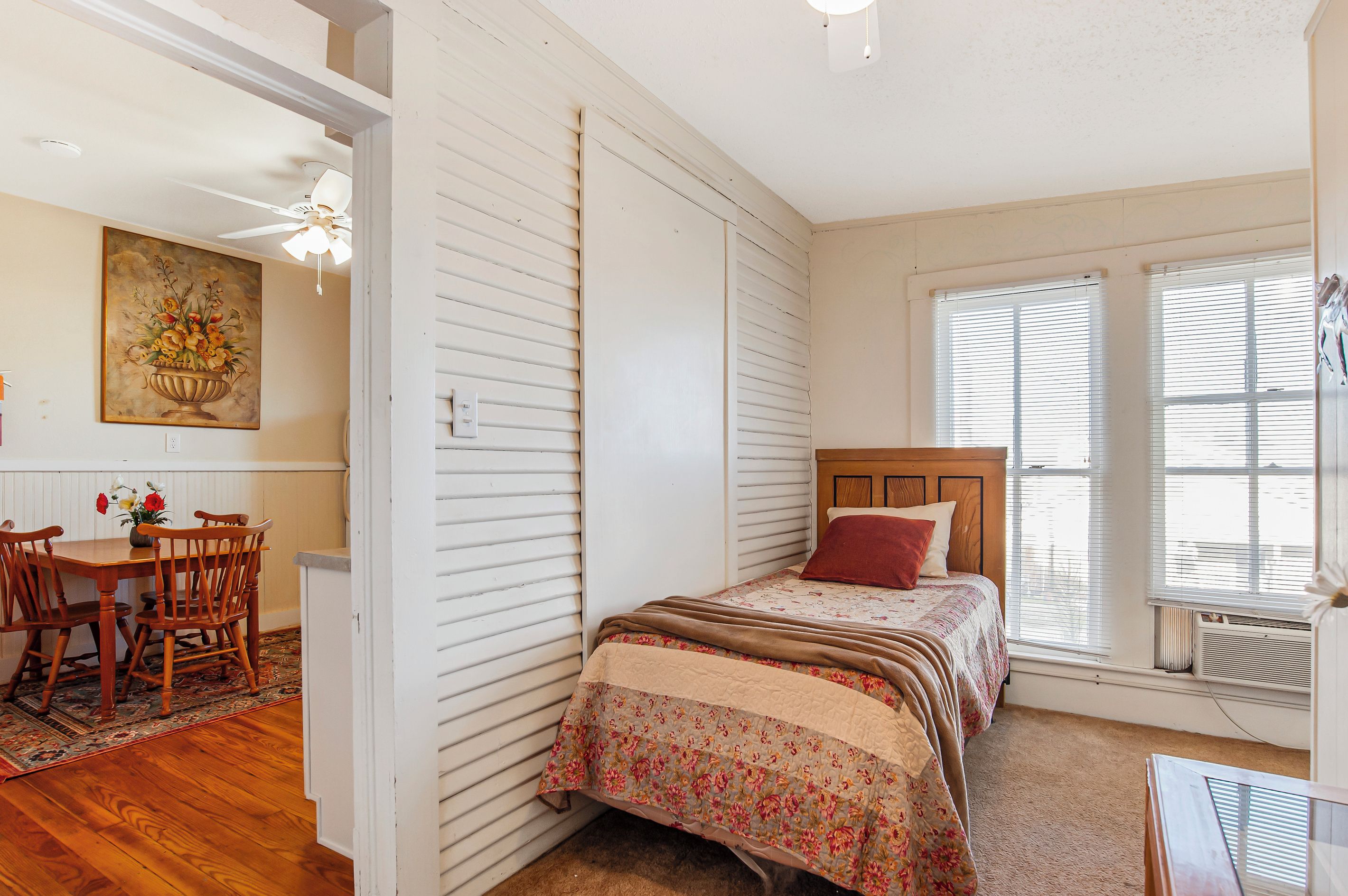 A bedroom with a bed, a nightstand, a window with blinds, and a painting on the wall.