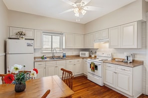 A kitchen with white cabinetry, a wooden dining table, and a ceiling fan.