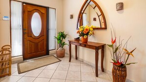 A wooden door with a glass panel, a wooden console table with a vase of flowers, a potted plant, a mirror, and a wooden chair.