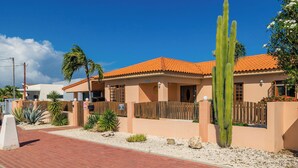 A two-story building with a red-tiled roof, a wooden fence, and a variety of desert plants.