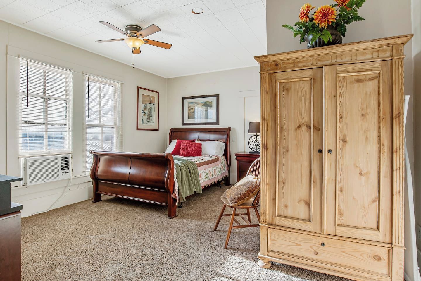 A bedroom with a bed, a wooden wardrobe, a ceiling fan, and a window with blinds.