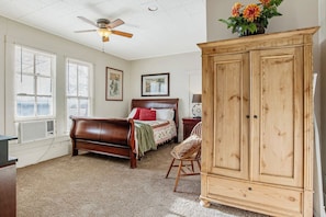 A bedroom with a bed, a wooden wardrobe, a ceiling fan, and a window with blinds.