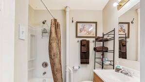 A bathroom with a shower curtain, toilet, sink, and towel rack. - Carriage Tarpley 5 | Queen Suite w/ Kitchen (Bandera)