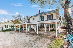 A two-story house with a covered porch and a dirt driveway. - Carriage Tarpley 5 | Queen Suite w/ Kitchen (Bandera)