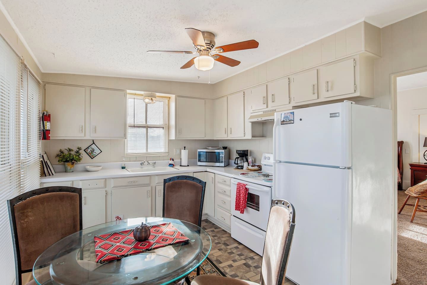 A kitchen with white cabinets, a microwave, a refrigerator, a ceiling fan, and a dining table with chairs.