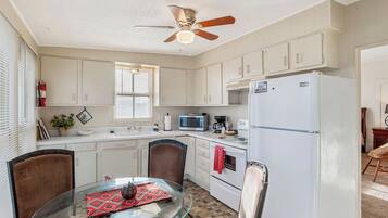 A kitchen with white cabinets, a microwave, a refrigerator, a ceiling fan, and a dining table with chairs.
