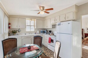 A kitchen with white cabinets, a microwave, a refrigerator, a ceiling fan, and a dining table with chairs. - Carriage Tarpley 5 | Queen Suite w/ Kitchen (Bandera)