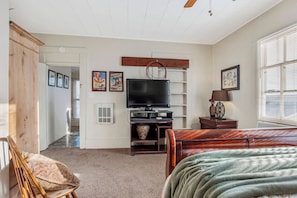 A bedroom with a bed, a TV, a wooden cabinet, and a window with blinds. - Carriage Tarpley 5 | Queen Suite w/ Kitchen (Bandera)