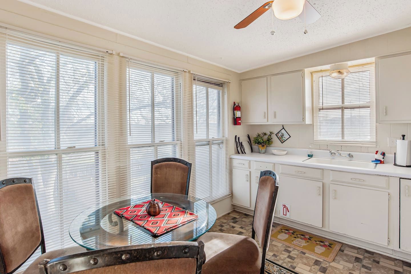 A dining area with a glass table, four chairs, and a ceiling fan.