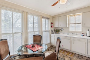 A dining area with a glass table, four chairs, and a ceiling fan.