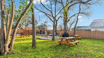 A backyard with picnic tables, a barbecue grill, and a stone fireplace.