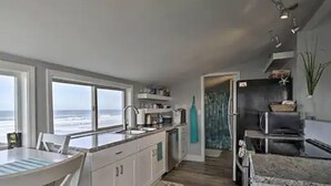 Una cocina moderna con vista al océano, armarios blancos y un comedor también con vistas.
