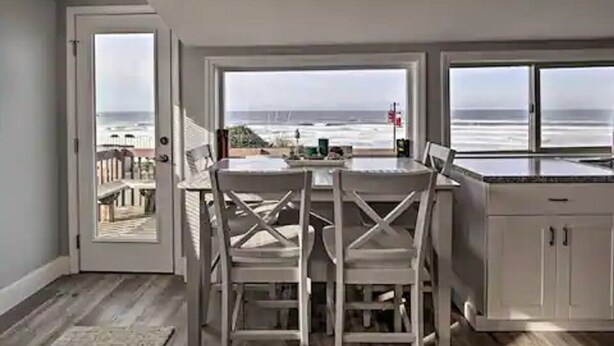 Una cocina con vista al océano, una mesa de comedor con sillas y una encimera blanca.