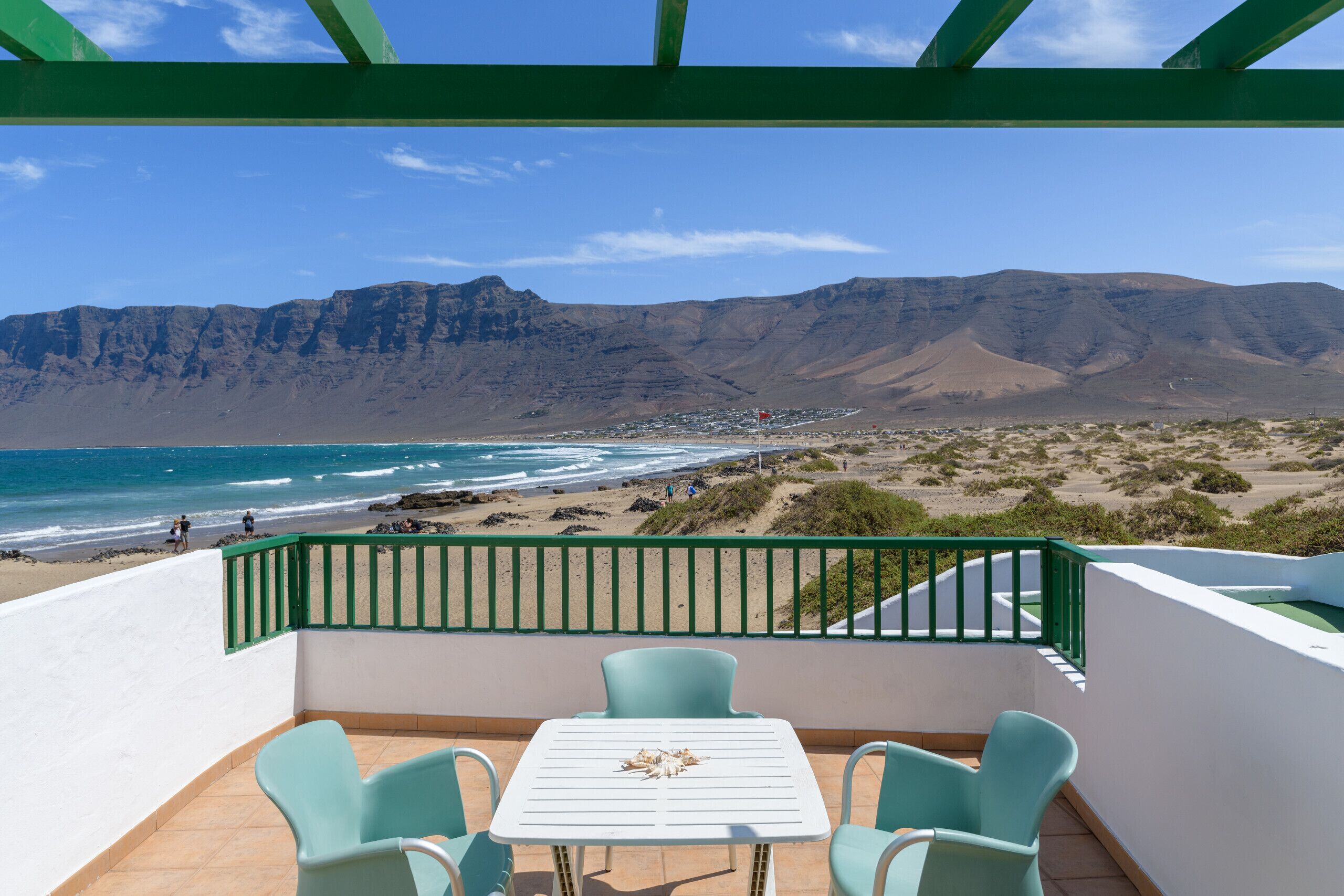 A balcony with a table and chairs overlooking a beach and mountains.