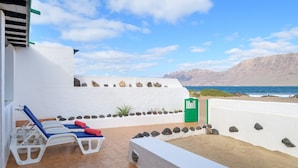 A terrace with two sun loungers, a green trash bin, and a view of the sea and mountains. - Caracolillos House, Famara Surf Beach (Famara)