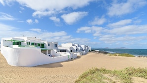 A row of white buildings with green accents on a sandy beach, overlooking the sea. - Caracolillos House, Famara Surf Beach (Famara)