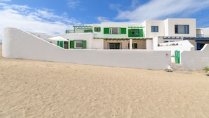 A coastal building with a white facade, green shutters, and a balcony. - Caracolillos House, Famara Surf Beach (Famara)