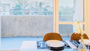 Une table à manger dressée pour deux personnes, avec vue sur le paysage urbain à travers une grande fenêtre.