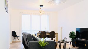 Un salon moderne avec un canapé gris, une table à manger avec des chaises, un téléviseur et une plante posée sur une petite table.