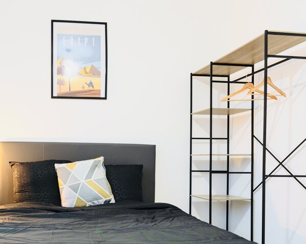 A bedroom with a bed, a hanging light, a framed picture, and a wooden shelf unit.