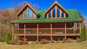 A log cabin with a green roof, a stone foundation, and a wooden deck.